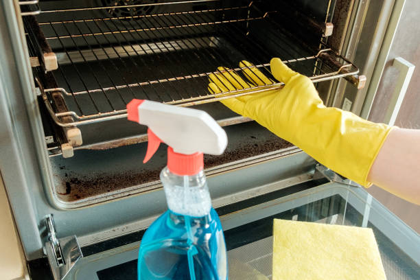 istock Man's hand in yellow rubber glove with rag cleaning kitchen oven 657102880