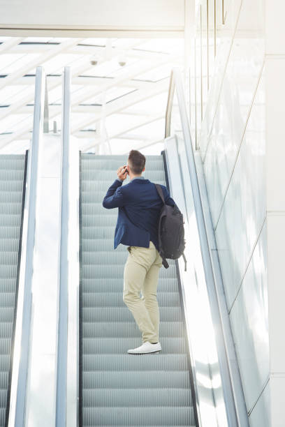 istock business man from behind standing on escalator on phone call 657110440