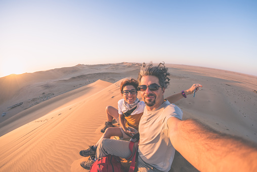 Adult couple taking selfie on sand dunes in the Namib desert, Namib Naukluft National Park, main travel destination in Namibia, Africa. Fisheye view in backlight, toned image.