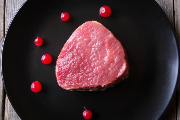 Fresh game meat on black plate and wooden table