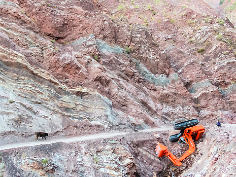 Carrying Excavator at the mountain road - Accident and excavator upside down - Excavator overturned near the cliff - very dangerous condition with unrecognizable people and cow