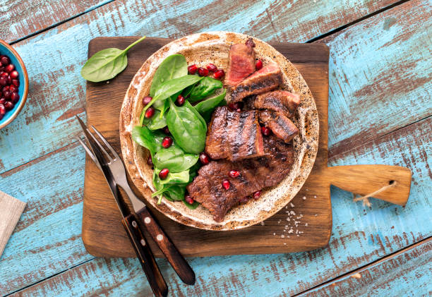 istock Beef steak grilled with spinach leaves and pomegranate in a plate on a blue wooden table. Rustic style 657146112