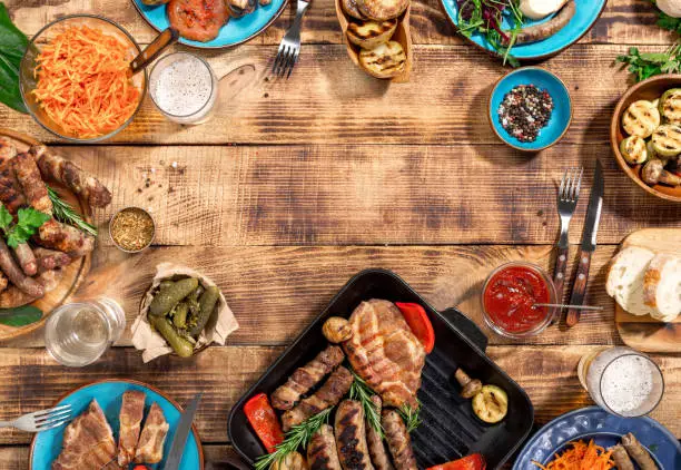 Photo of Appetizing barbecued steak, sausages and grilled vegetables on a wooden picnic table with copy space