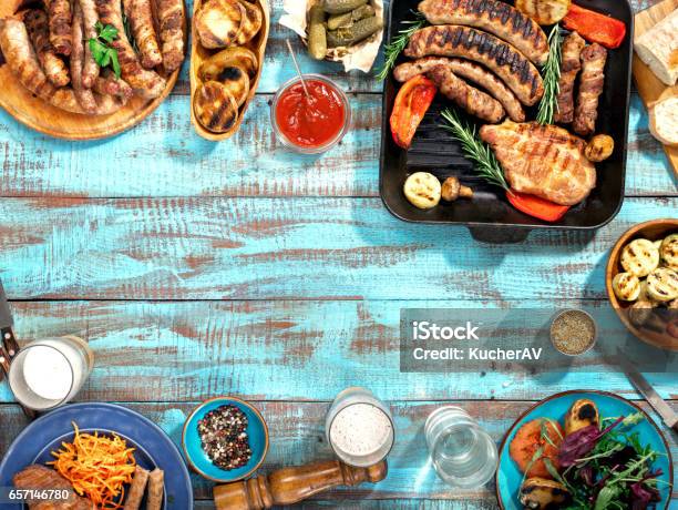 Verschiedenes Essen Zubereitet Auf Dem Grill Auf Dem Blauen Holztisch Auf Einem Sonnigen Tag Gegrilltes Steak Bratwürste Gegrilltem Gemüse Und Lagerbier Stockfoto und mehr Bilder von Gartengrill