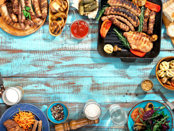 diferentes alimentos cozidos na grelha sobre a mesa de madeira azul em um dia ensolarado, bife grelhado, linguiça grelhada, legumes grelhados e cerveja lager - zucchini vegetable food food and drink - fotografias e filmes do acervo