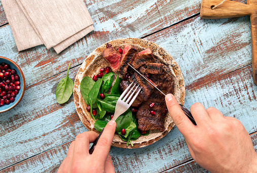 Man eats a beef grilled steak on wooden table. Rustic style, top view