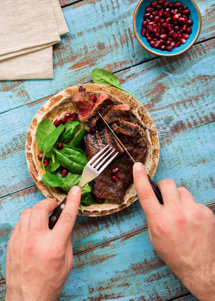 istock Man eats a beef grilled steak with spinach and pomegranate on wooden table. Rustic style, top view 657147196