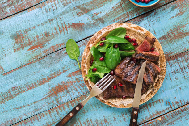 istock Plate with grilled steak, spinach leaves and pomegranate on a wooden blue table with copy space 657147442