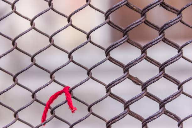 istock Rusty steel chain link or wire mesh as boundary wall. Red thread. There is still concrete block wall behind the mesh. 657153320