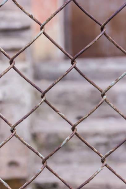 istock Rusty steel chain link or wire mesh as boundary wall. There is still concrete block wall behind the mesh. 657153354
