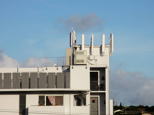 Cell Towers line top of white Apartment Building in Honolulu, Oahu, Hawaii.  With clouds in the sky and power lines in the background.