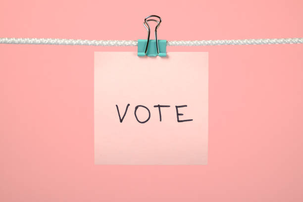 istock Pink paper note on clothesline with text Vote over colorful background 657163782