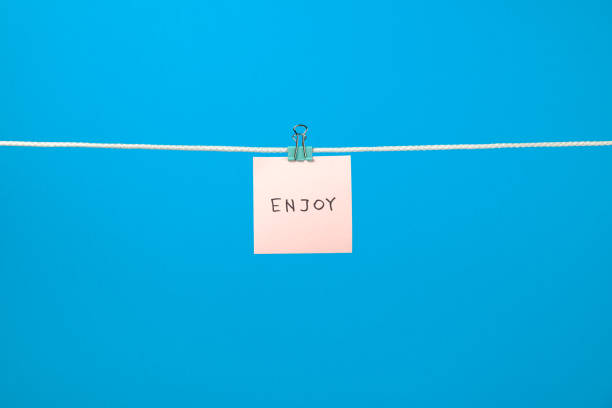 istock Pink paper note on clothesline with text Enjoy over colorful background 657163812