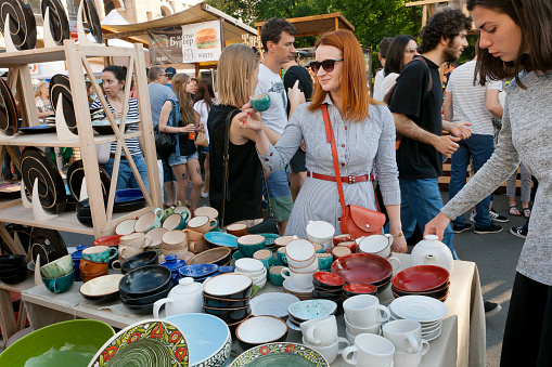 Kyiv, Ukraine - June 4, 2016: Young women choosing pottery on the stand of crowded weekend street fair on June 4, 2016. Kiev is the 8th most populous city in Europe.