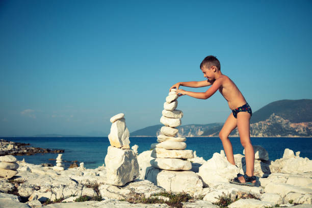 Little boy making huge stack of rocks in balance on the rocky beach