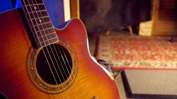 An Acoustic Guitar on a Dark Background in a Home environment, with the Guitar in focus and the Background out of focus.
