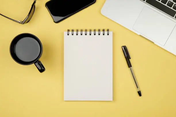 Modern office desk table with laptop, blank notebook page for input the text in the middle and other supplies. Top view, flat lay