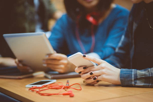 Group of female students together using a mobile phone and digital tablet in class. Focus on woman hands holding smart phone.