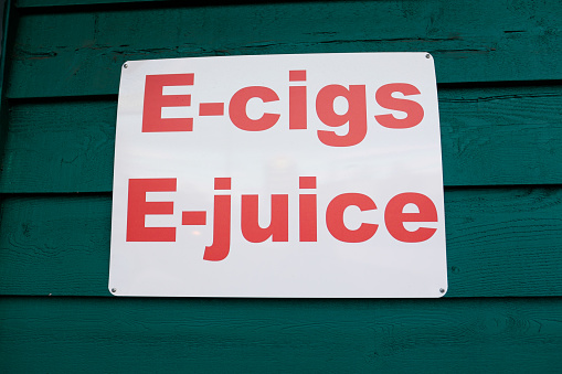 Sign on a green building says e-cigs and e-juice showing customers what they sell at this new vaping store.