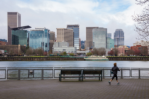 Portland, DeepMeta.Shared.Country: The city skyline of Portland across the Willamette River as a runner jogs by on the SE waterfront path downtown.