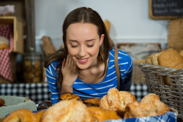 sonriente mujer que huele un pan en el mostrador - smelling bread bakery women fotografías e imágenes de stock