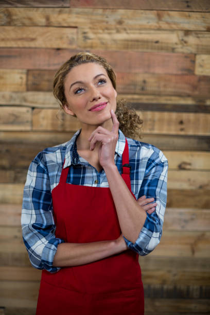 istock Thoughtful waitress standing against wooden wall 657264628