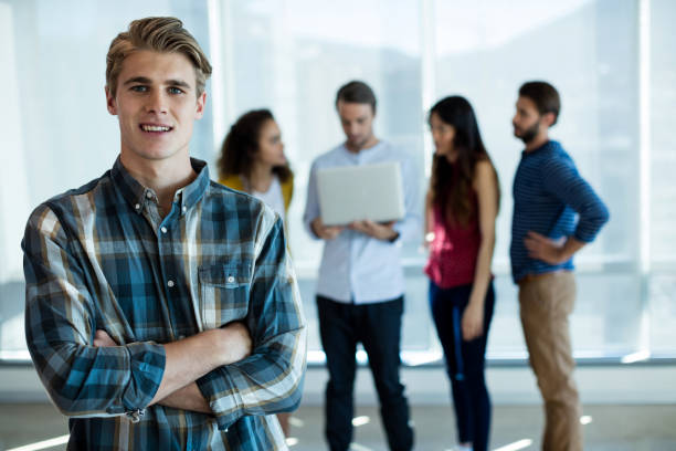 istock Man standing with arms crossed in office while colleague discussing in background 657296140
