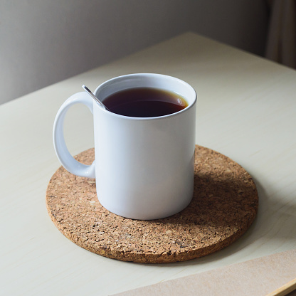 White cup of black tea and cork coaster on wooden table