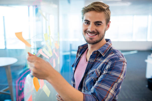 istock Smiling man touching sticky note on glass wall in office 657330712