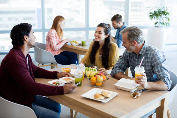Creative business team discussing while having meal Creative business team discussing while having meal in office cafeteria photos stock pictures, royalty-free photos & images