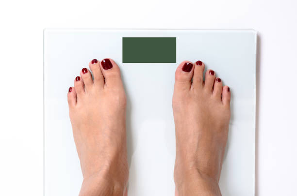 Close-up of woman feet with red nail polish standing on white weight scales with green screen