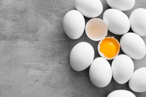 White eggs on a concrete table. One egg is cracked and you can see the yellow yolk