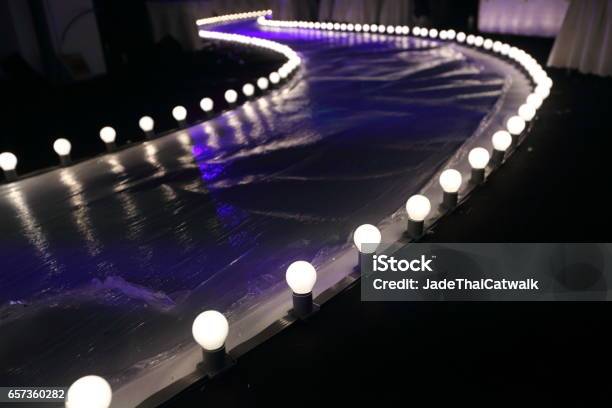 Empty Runway Fashion Show With Ball Glowing Lighting Along Walk Way With Plastic White Floor In The Dark Stock Photo - Download Image Now