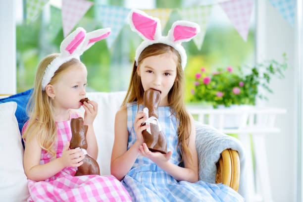 istock Two cute little sisters wearing bunny ears eating chocolate Easter rabbits 657368916
