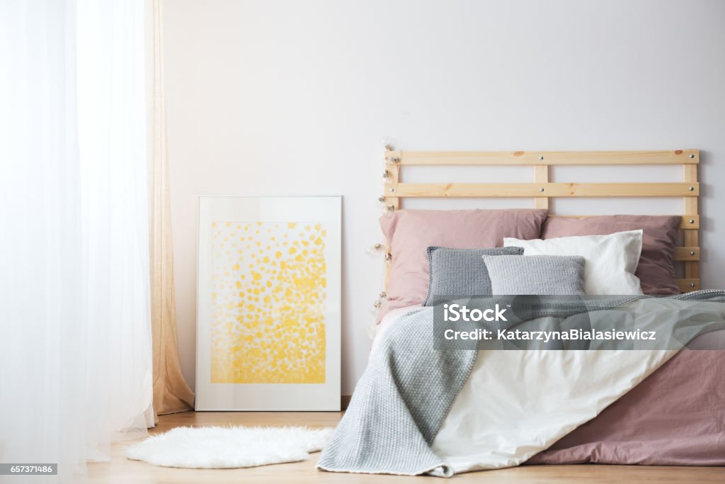 Bed, poster and rug King-size bed, yellow poster and white rug in cozy bedroom Apartment Stock Photo