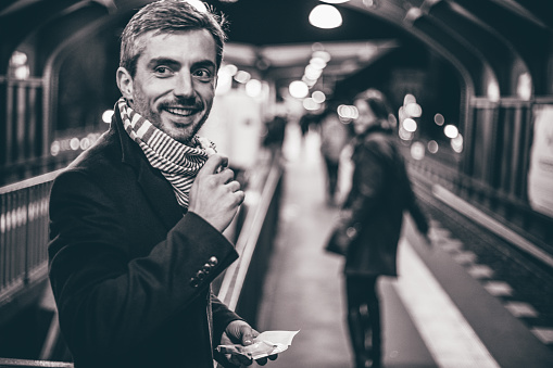 Man waiting for a train on the train station at night and eating chocolate