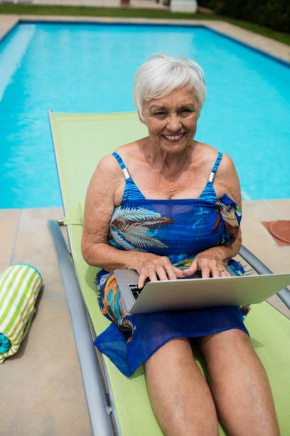 retrato de mujer senior con laptop en butaca - outdoor chair beach chair sarong fotografías e imágenes de stock