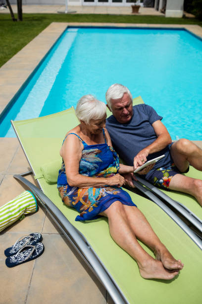 senior pareja con tableta digital en silla de salón - outdoor chair beach chair sarong fotografías e imágenes de stock