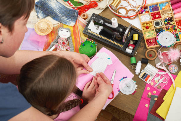 mother teaching daughter to sew doll clothes, top view, sewing accessories top view, seamstress workplace, many object for needlework, handmade and handicraft mother teaching daughter to sew doll clothes, top view, sewing accessories top view, seamstress workplace, many object for needlework, handmade and handicraft atelier fashion stock pictures, royalty-free photos & images