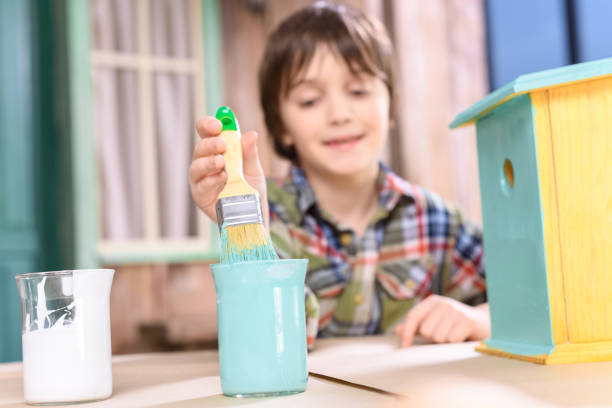 istock Cute smiling boy holding paintbrush while painting handmade birdhouse 657410818