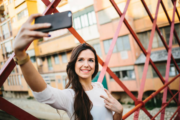 Young girl taking selfie on bridge Young smiling woman doing self portrait with 'peace' gesture on bridge. taken on mobile device stock pictures, royalty-free photos & images