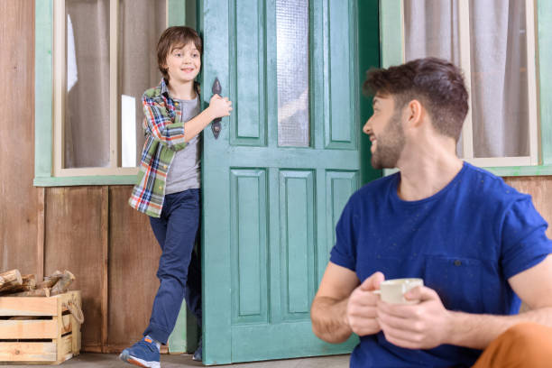 istock smiling man sitting on porch with tea cup and looking at boy behind 657421866
