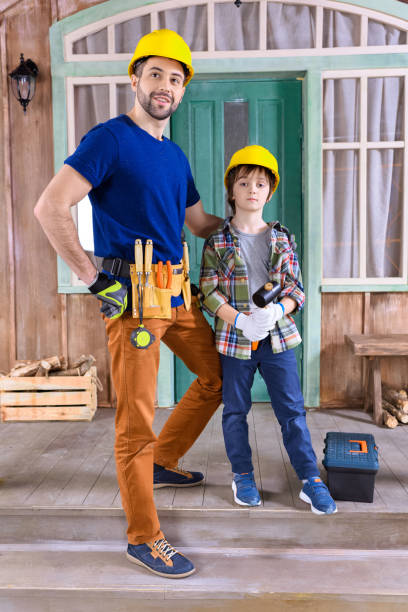 father and son in helmets with building tools standing on porch