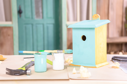 Close-up view of handmade small birdhouse with paints and tools on table