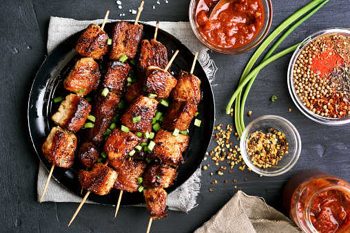 Bbq meat on wooden skewers on plate, top view