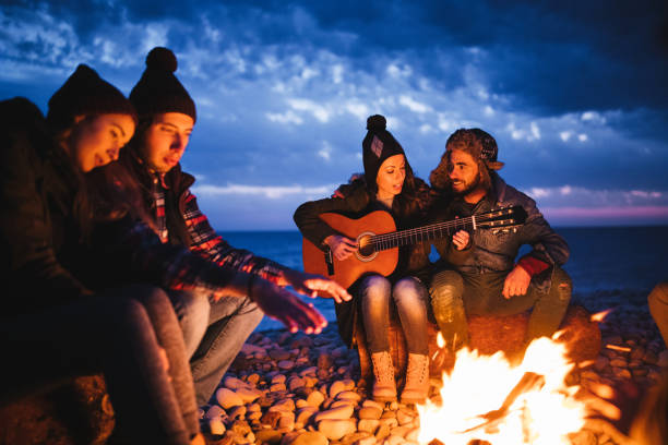 istock Friends sitting around a campfire at the beach playing guitar 657429544