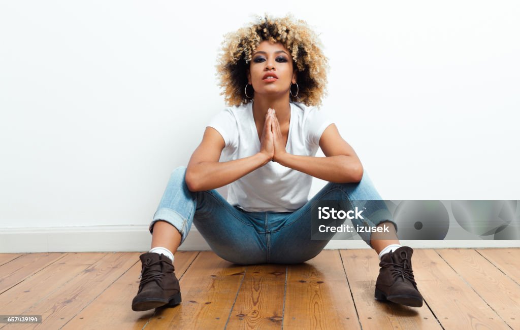 Confident afro american young woman sitting on the floor Portrait of beautiful afro american young woman sitting on the floor, looking at camera. Fashion Model Stock Photo