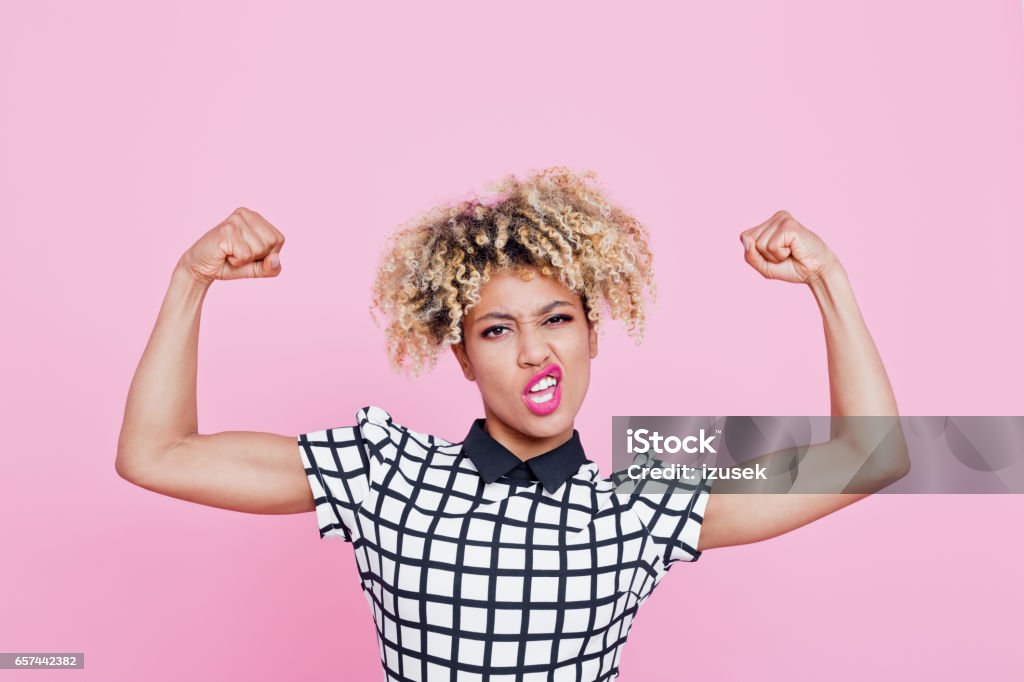 Strong afro american young woman flexing muscles Studio portrait of strong afro american young woman flexing muscles. Pink background. Women Stock Photo