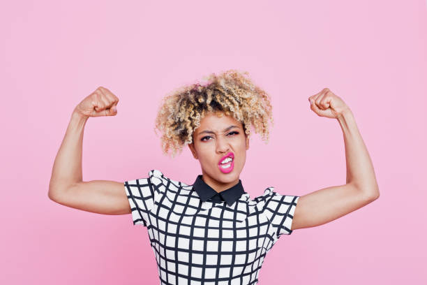 Strong afro american young woman flexing muscles Studio portrait of strong afro american young woman flexing muscles. Pink background. bicep stock pictures, royalty-free photos & images