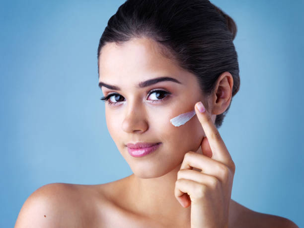 You've gotta take care of your skin Studio portrait of a beautiful young woman applying face cream against a blue background face cream stock pictures, royalty-free photos & images